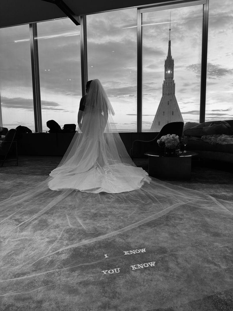 Shot of the bride's veil sprawling behind her with a view on a building through the window, in black an white.