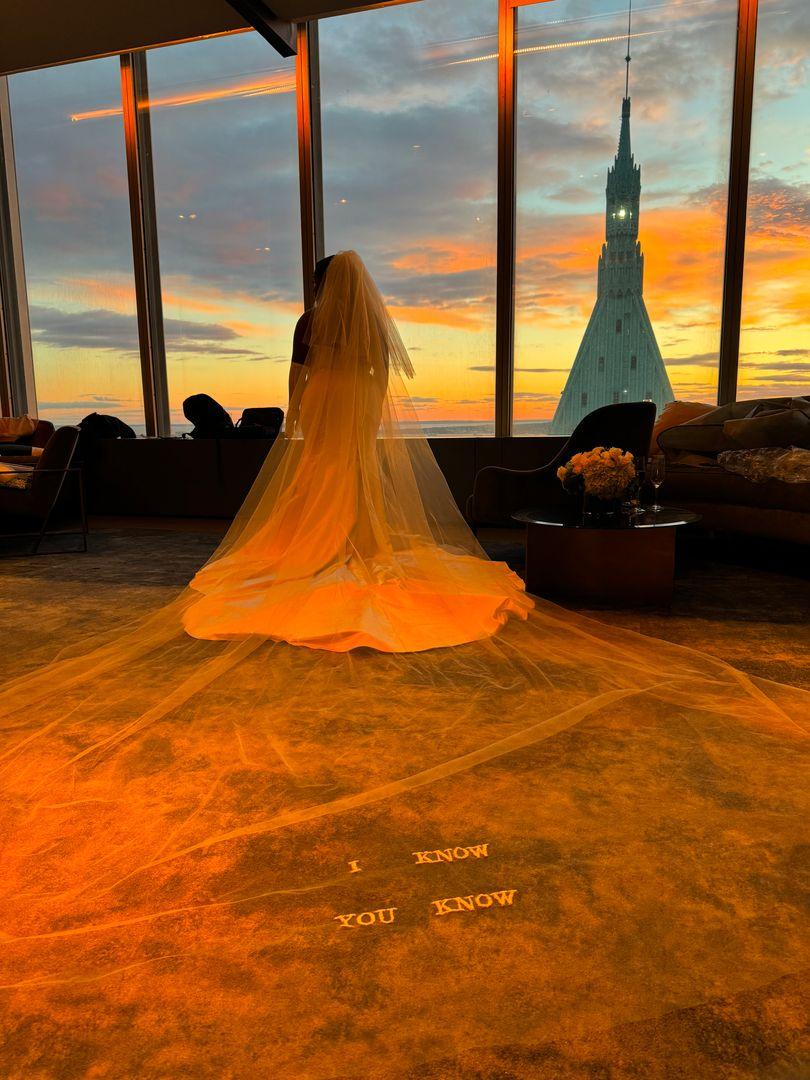 Shot of the bride's veil sprawling behind her with a view on a building through the window.