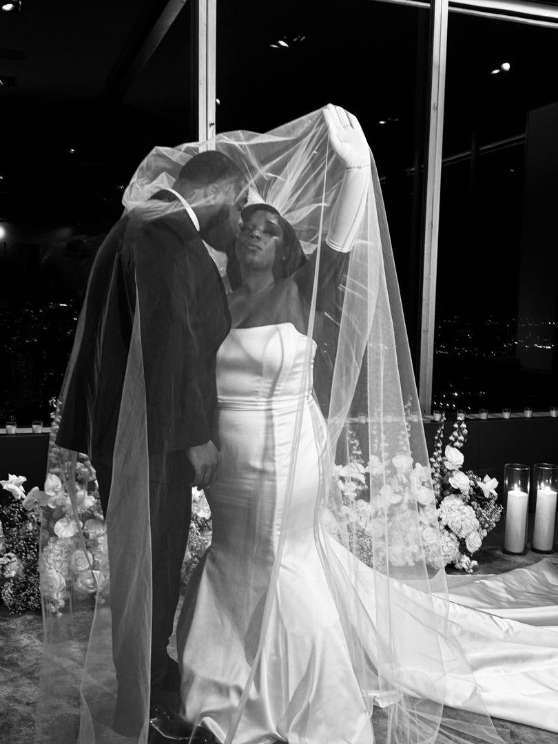 Groom kissing the bride under her veil, in black and white.