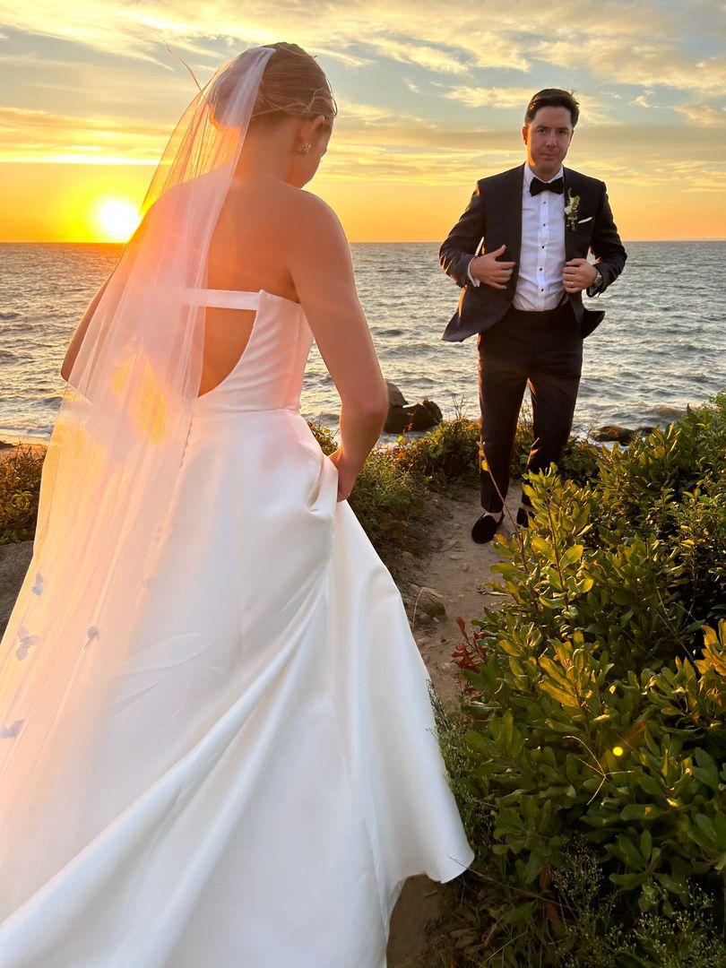 Bride walking towards the groom with the sunset and ocean in the background.